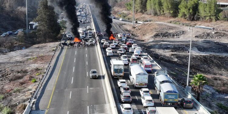 A drone photo shows protesters standing next to burning tires as they block Israel's main highway connecting Jerusalem and Tel Aviv near Latrun, Israel, after families of hostages have called for a nationwide strike to demand the return of all hostages and an end to the war in Gaza, August 17, 2025. REUTERS/Stringer